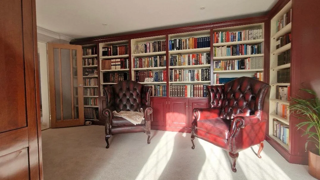 A fitted library with painted bookcases and two leather wing chairs
